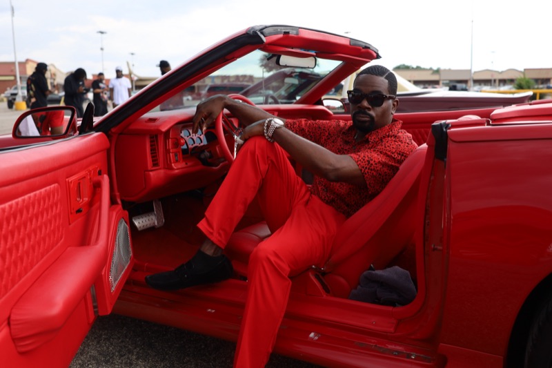 Don Chief in a red suit behind the wheel of a red convertible